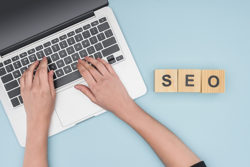 Top view of woman typing on laptop keyboard on light blue background seo content writing services
