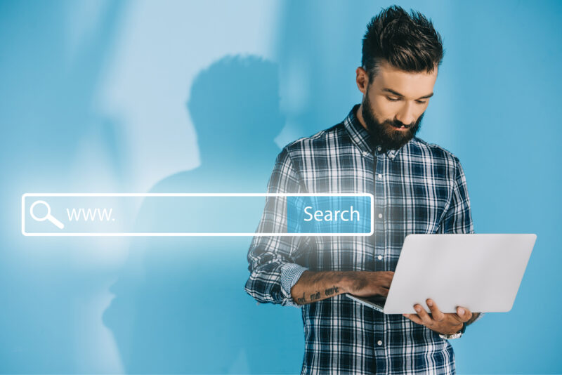 bearded developer using laptop, on blue with website search bar man using laptop to use AI search and understanding answer engine optimization